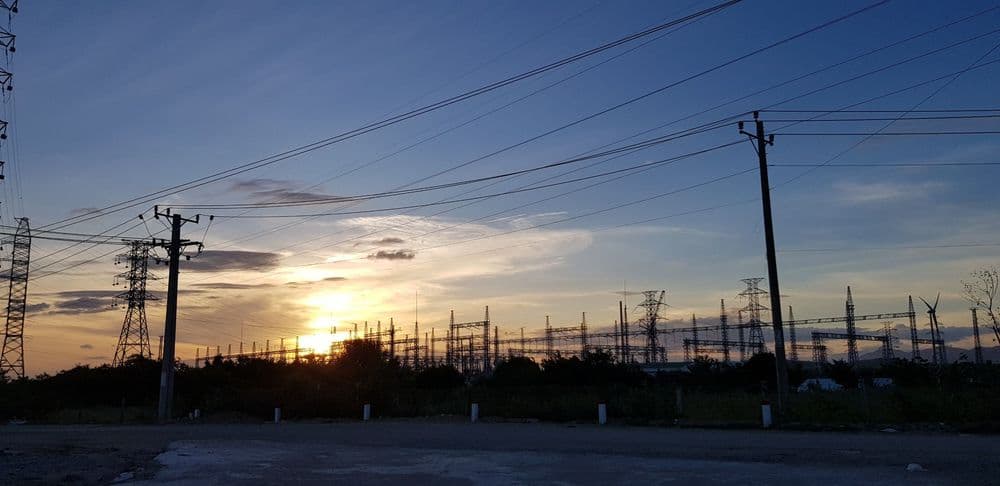 Sunset behind power lines and an electrical substation, silhouetted against the sky.