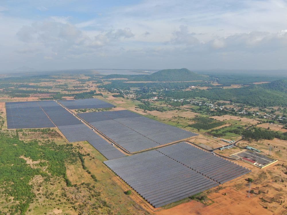 A sprawling solar farm with countless photovoltaic panels under a partly cloudy sky.