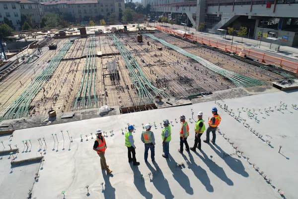 Group of construction workers stand on a concrete deck overlooking an active site with rebar.