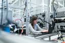 Female engineer uses a laptop amidst intricate wiring and machinery in a modern factory.