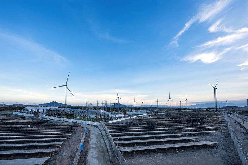Wind turbines and vast rows of solar panels under a blue sky, signifying renewable energy.
