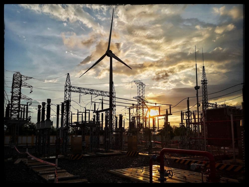 Wind turbine and electrical substation at sunset, showing renewable energy infrastructure.
