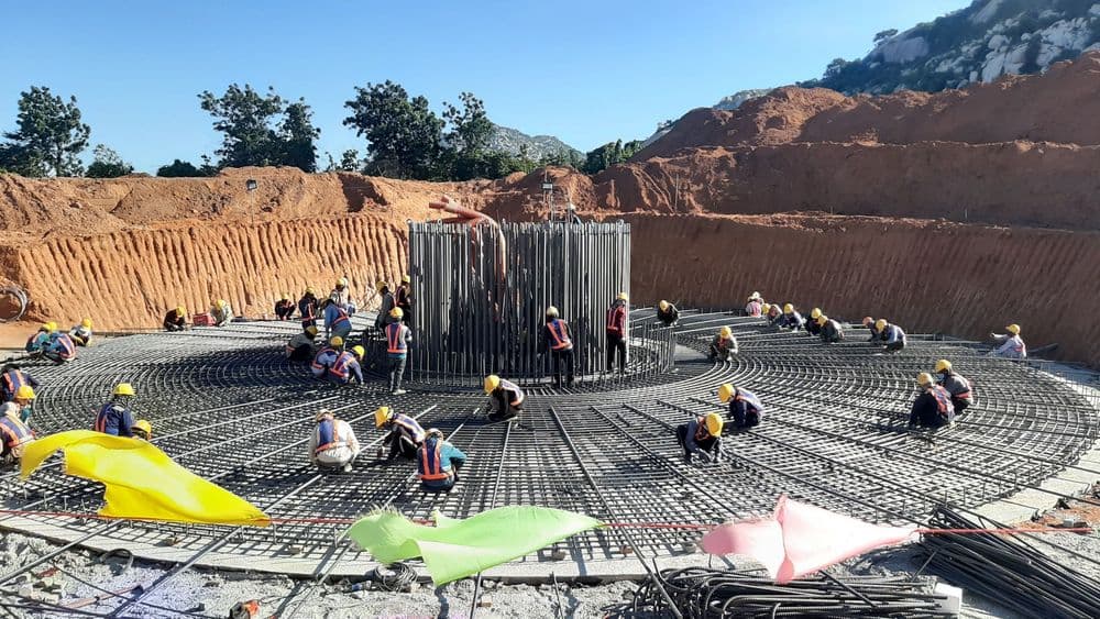 Workers construct a large circular foundation with extensive rebar at an outdoor site.