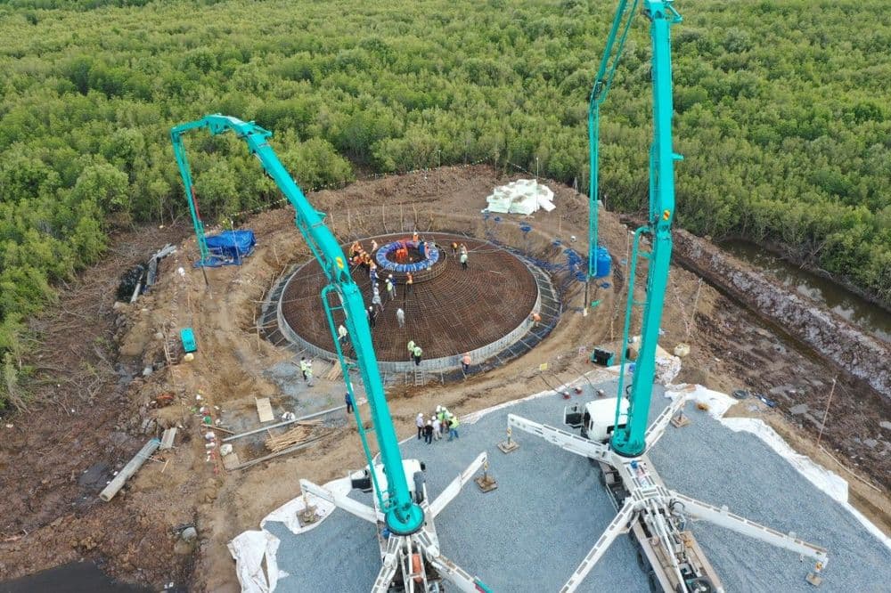 Aerial view: two concrete pumps pour into a circular foundation at a construction site.