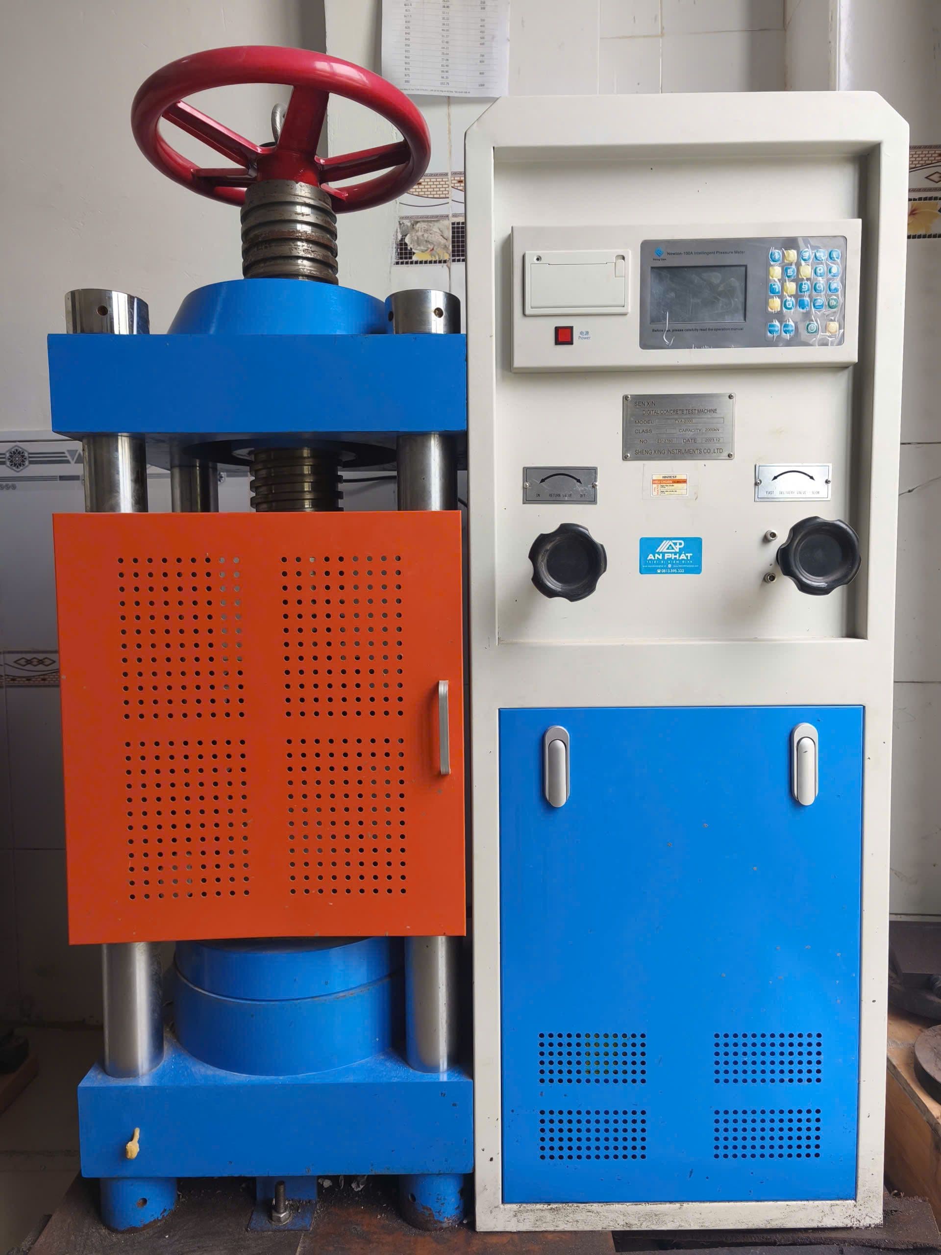 Hydraulic universal testing machine with orange and blue components, and a red hand wheel.